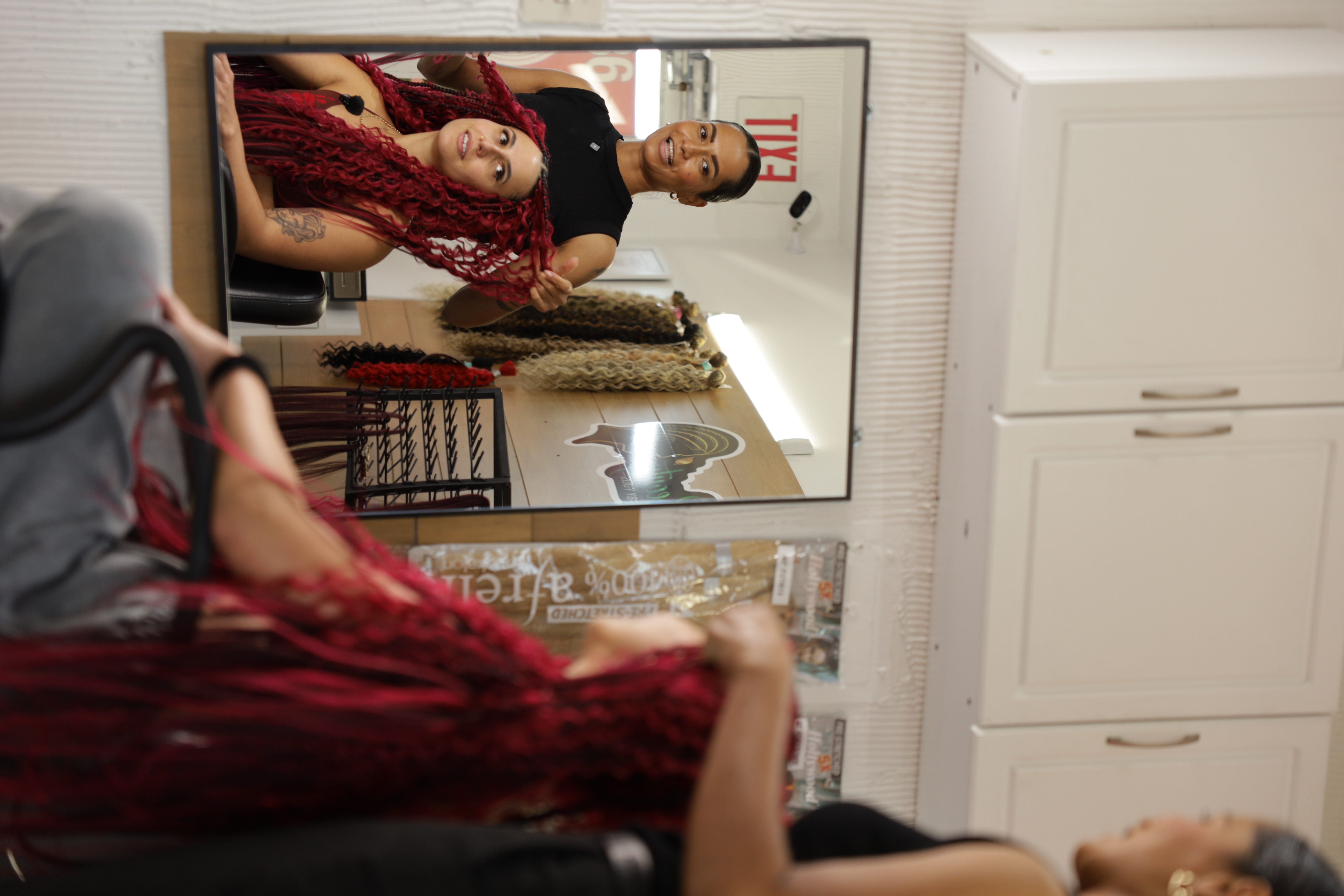 Mirror shot of Yulis braiding red braids on a young woman
